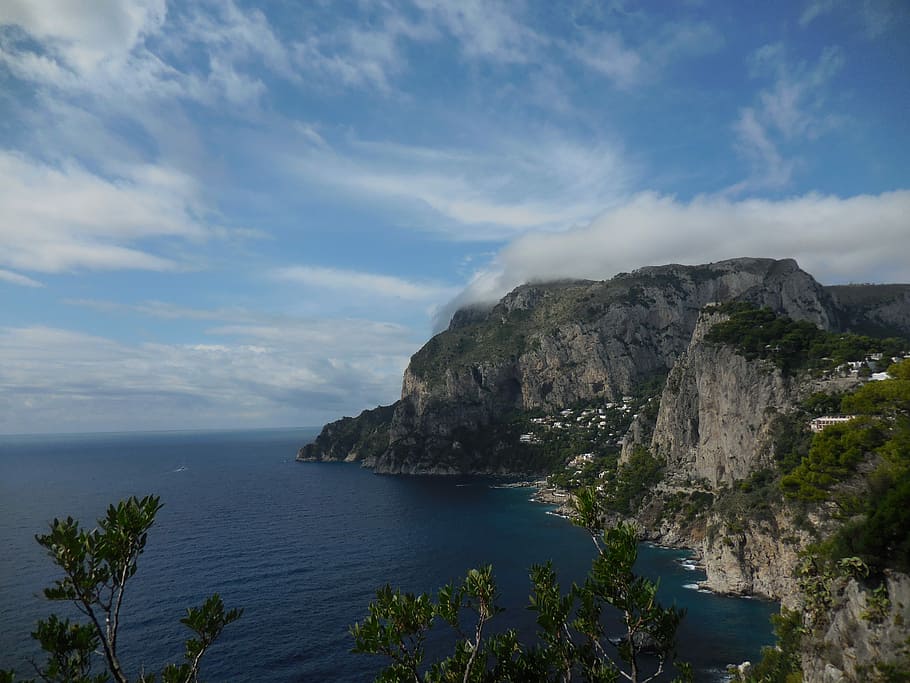 cliff surrounded with bushes under cirrus clouds, landscape photography of mountain near body of water HD wallpaper