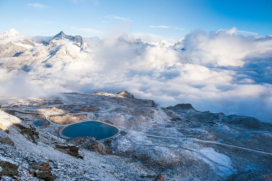 body of water surrounded by mountain under cloudy sky, aerial view photography of snow mountain during daytime HD wallpaper