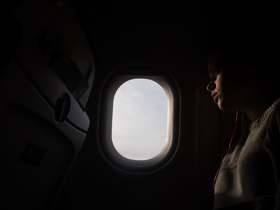 woman using red in-ear headphones while riding airplane, woman sitting in airplane beside window HD wallpaper
