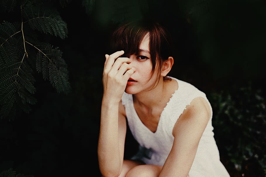 vignette photography of woman in white sleeveless dress, woman sitting while holding her nose