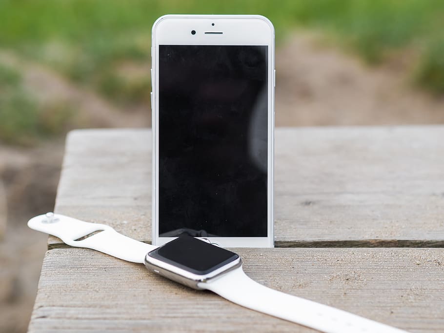 silver aluminum Apple Watch beside silver iPhone 6 on table outdoors during day