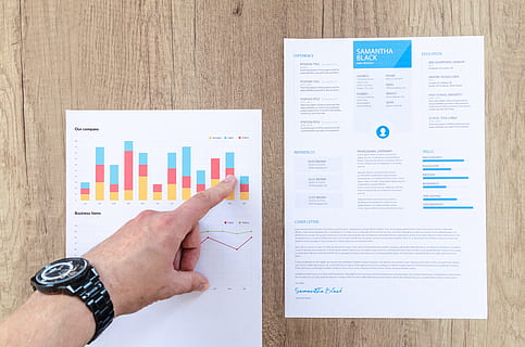 person pointing two white data papers on wood surface, chart HD wallpaper