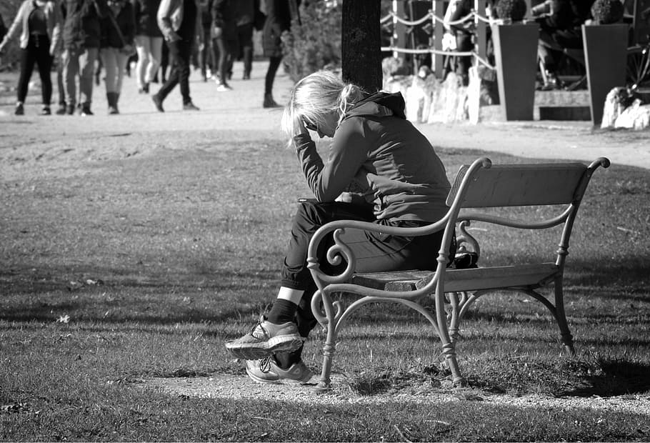 grayscale photography of woman sitting on bench while resting her hand on head