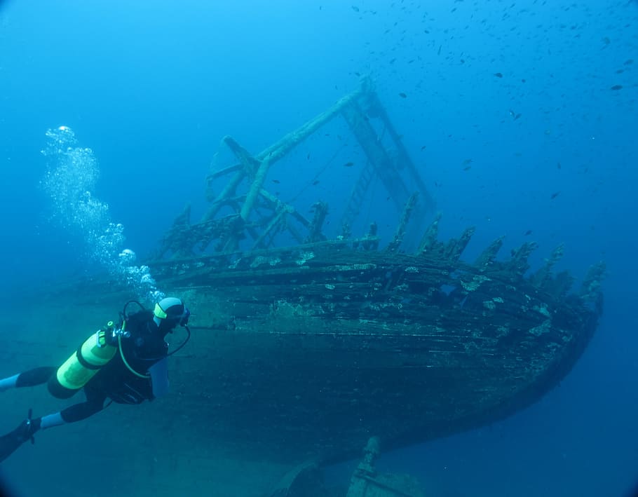 man diving underwater with brown wooden ship, croatia, mediterranean