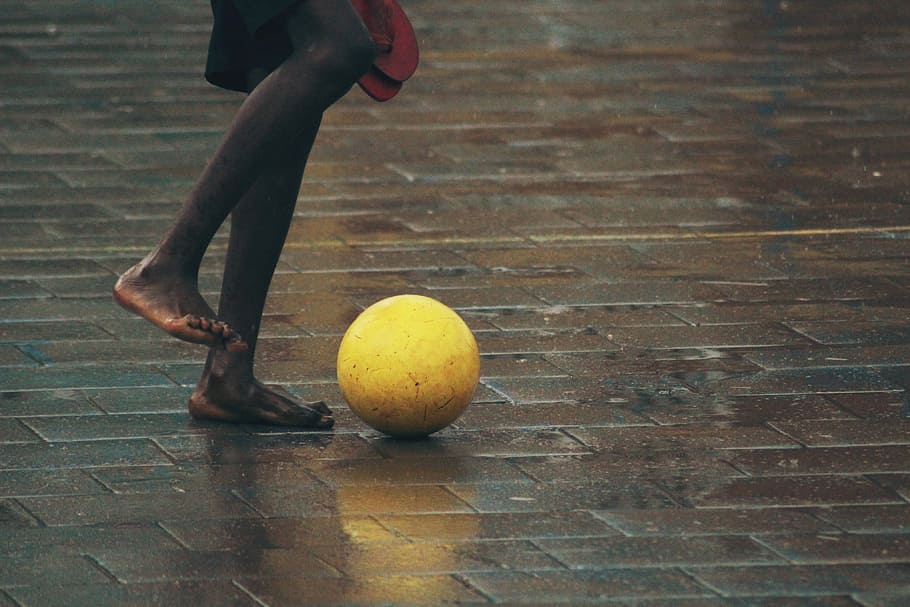person standing gray brick floor about to kick ball, person standing in front of yellow ball, HD wallpaper
