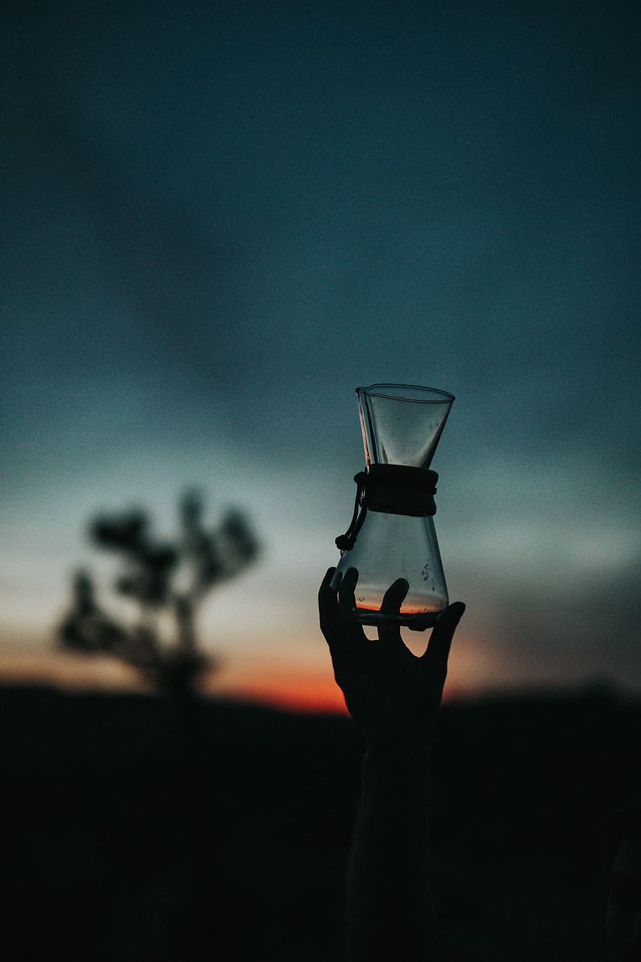 tilt shift lens photography of clear glass vase, silhouette photo of left human hand holding clear glass container HD wallpaper