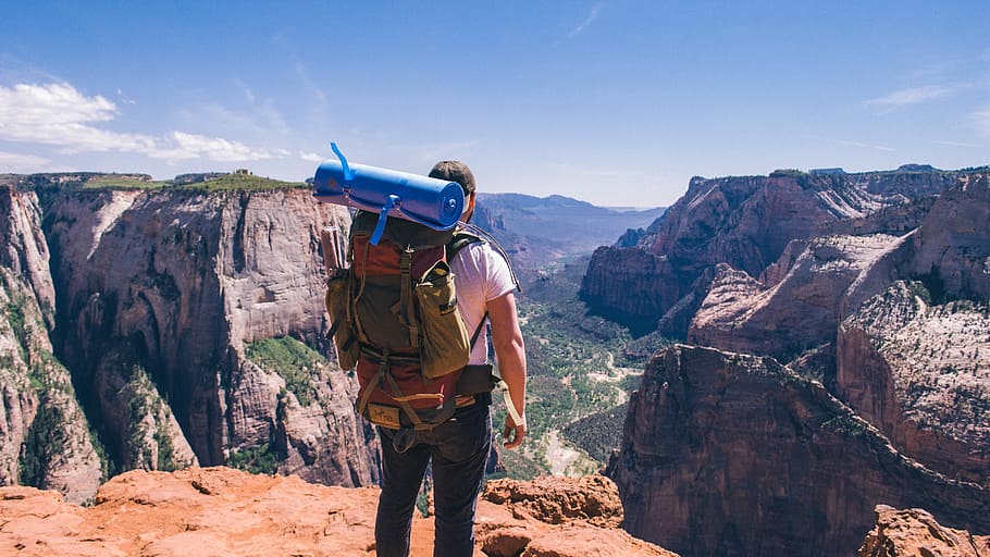 man standing on top of mountain facing mountain view, man standing on cliff wearing trek backpack HD wallpaper
