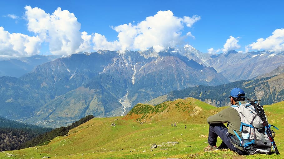 man sitting on green lawn looking at the mountain at daytime