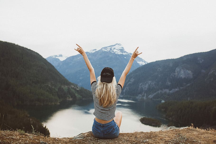 woman sitting on cliff raising both hands, woman sitting enjoying mountain and body of water HD wallpaper