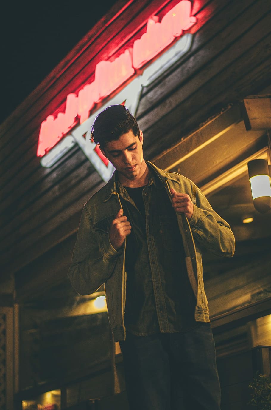 man holding his brown jacket and standing in front of brown concrete storefront low-angle photo, man fixing his jacket HD wallpaper
