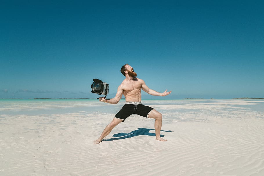 man holding camera on seashore, man holding gray and black LED light on desert HD wallpaper