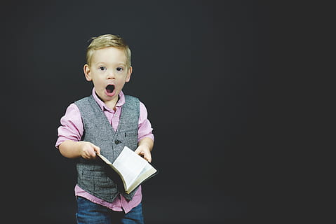 boy wearing gray vest and pink dress shirt holding book, boy holding opened book while opening his mouth HD wallpaper