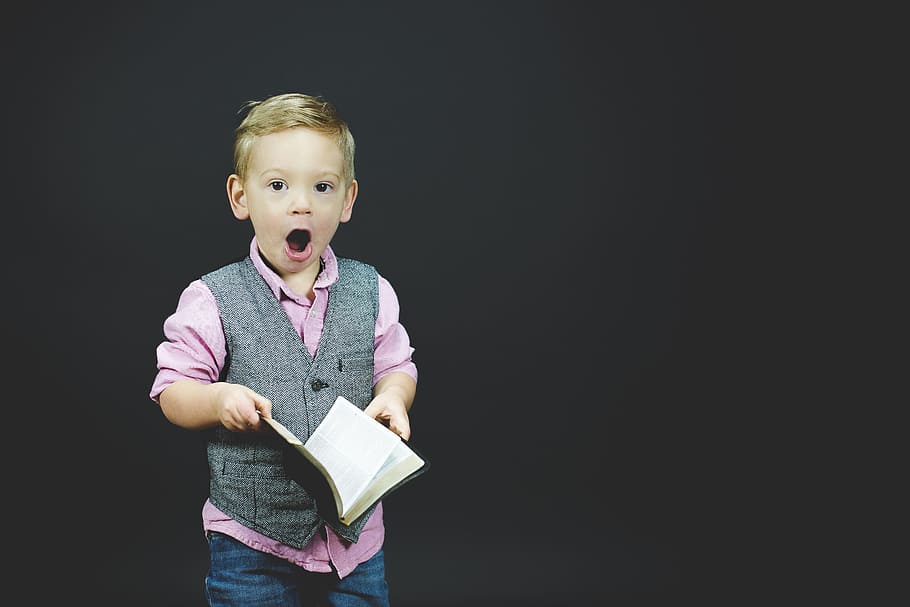 boy wearing gray vest and pink dress shirt holding book, boy holding opened book while opening his mouth HD wallpaper