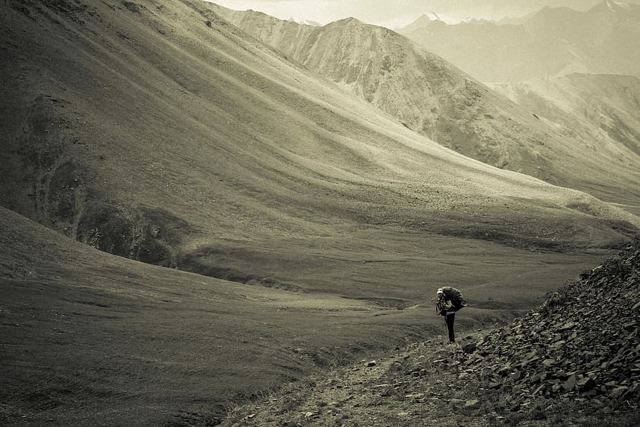 grayscale photo of person walking on mountain feet during daytime, man hiking near mountain at daytime HD wallpaper