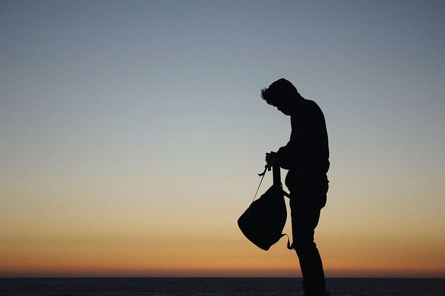 silhouette of man holding backpack during orange sunset, silhouette photo of man holding bag