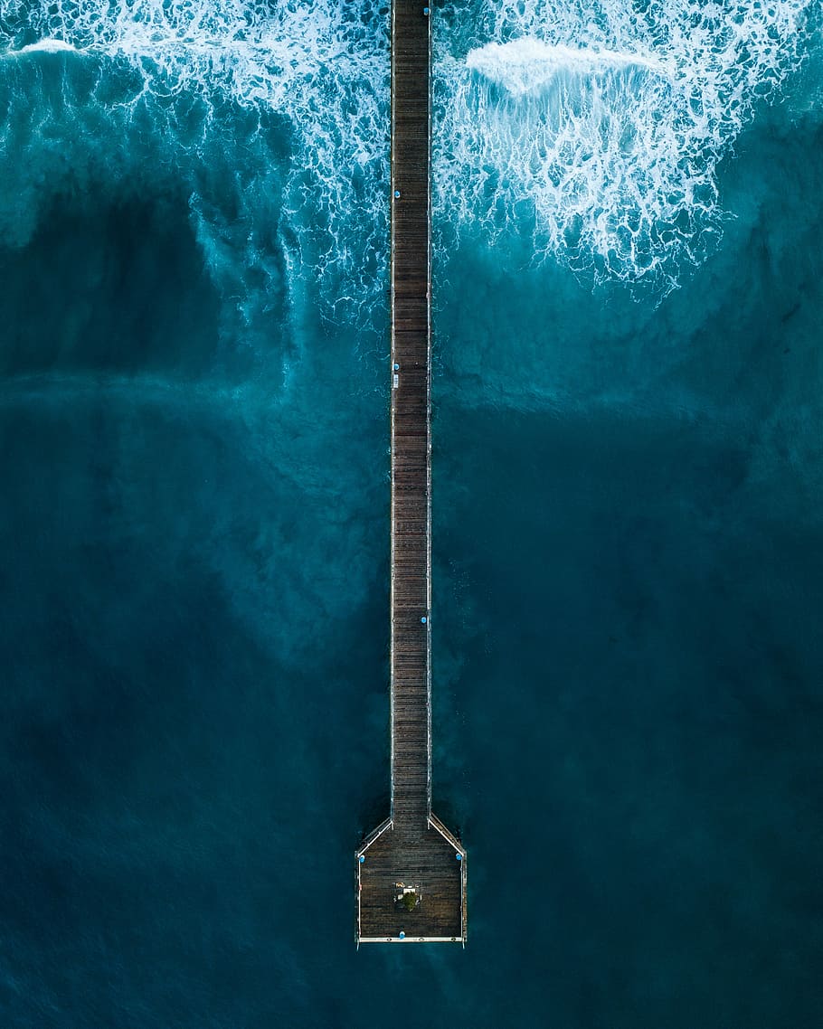 aerial photography of person standing on dock beside sea at daytime, bird's eye view of brown wooden pier