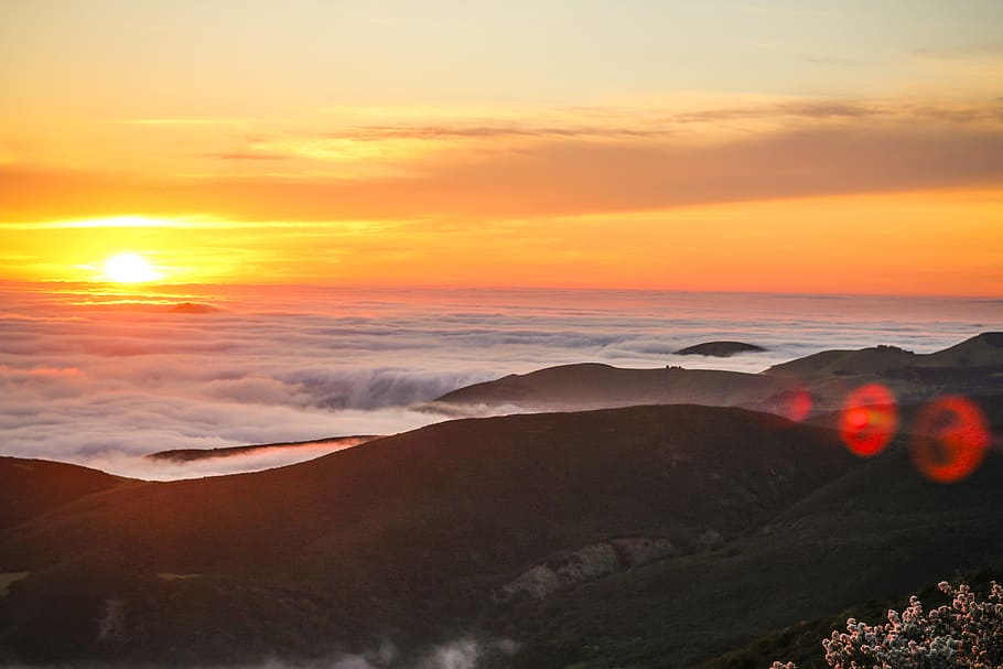 sun over the clouds and hill, mountain near body of water, sunrise HD wallpaper