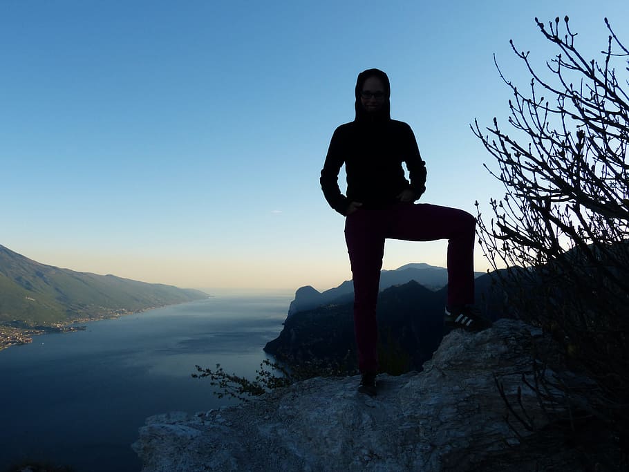silhouette of person standing on hill viewing body of water and mountain range HD wallpaper