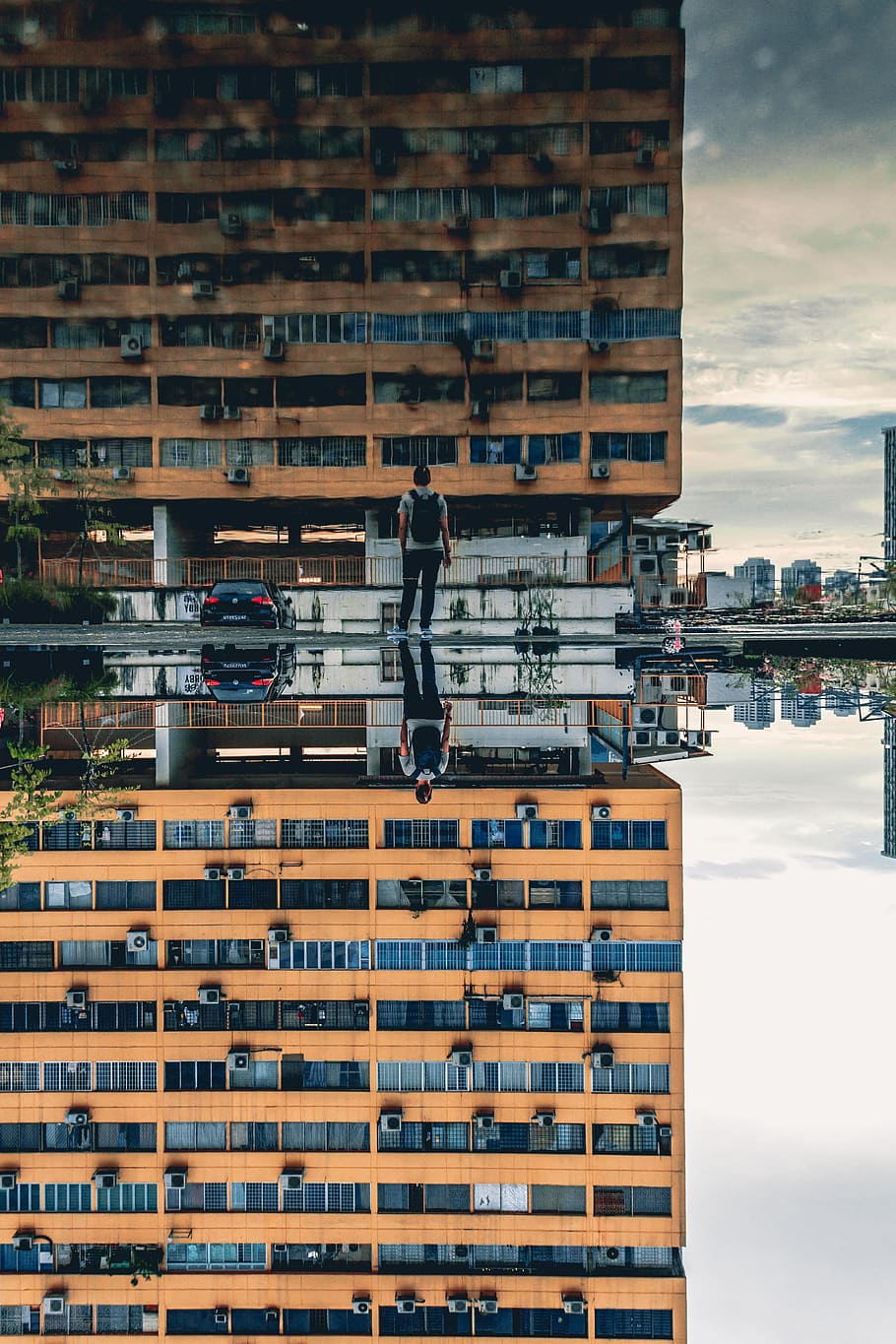 man standing in front of brown concrete high-rise building during daytime, brown concrete building and standing man reflecting through water HD wallpaper