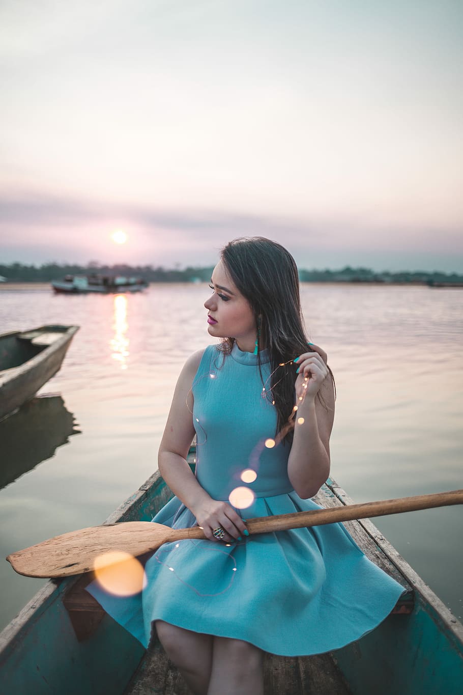 woman sitting on boat holding paddle, woman sitting on blue boat while holding brown wooden paddle on lap