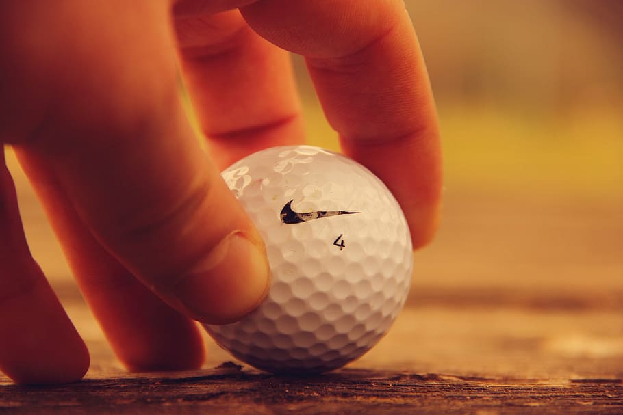 person holding white Nike golf ball, sports, hole, grass, field
