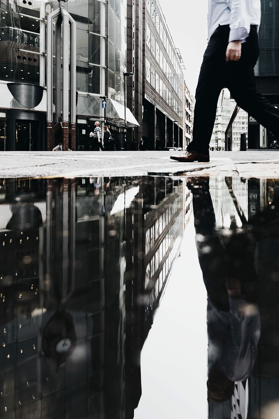 man walking near puddle of water casting reflection, man walking on street near buildings during daytime HD wallpaper