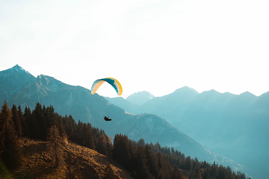person paragliding near mountain at daytime, person paragliding over brown leafed trees during daytime HD wallpaper