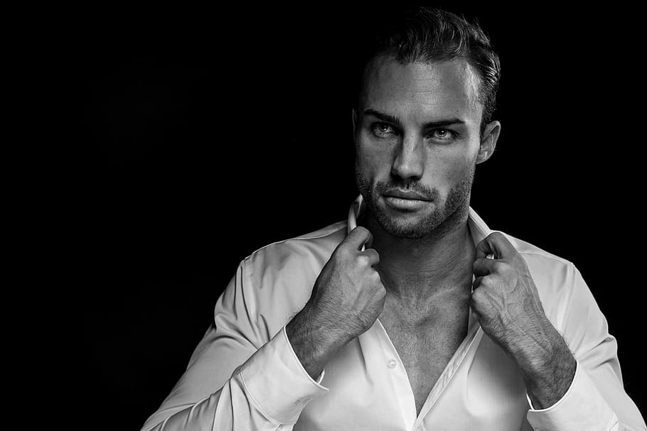 grayscale portrait of man wearing white dress shirt on black background, man wearing white shirt holding it's collar