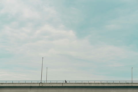 gray suspension bridge under white clouds during daytime, person walking on bridge HD wallpaper
