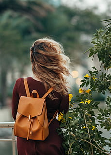 woman carrying brown leather backpack, selective focus photography of woman carrying brown leather backpack beside yellow flowers HD wallpaper