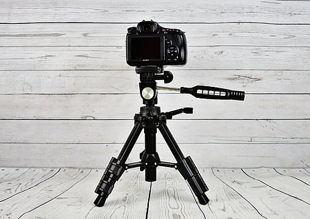 black camera with black tripod stand on white wooden surface HD wallpaper