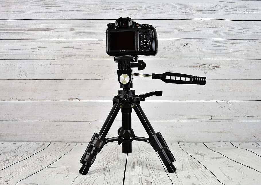 black camera with black tripod stand on white wooden surface HD wallpaper