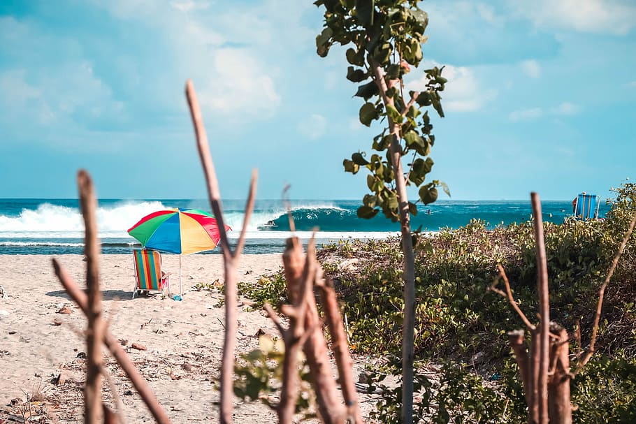 red, yellow, blue, and green parasol on seashore, umbrella in front of wave of sea HD wallpaper