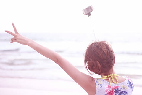 woman wearing white and red floral top wear using monogram to have selfie beside seashore during daytime HD wallpaper