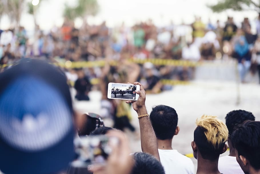 person holding white smartphone while taking photo, person holding smartphone focusing with people sitting in front HD wallpaper