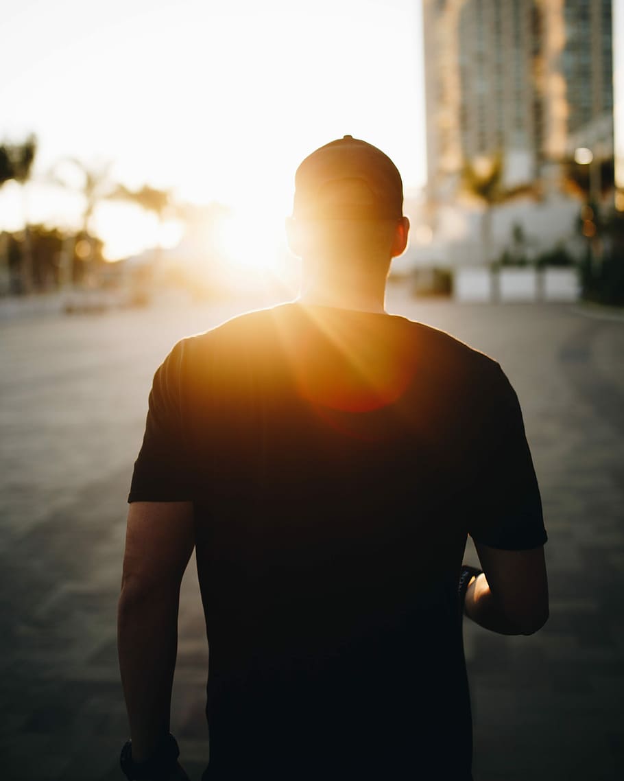 man in black shirt walking towards building, palm tree, pacific ocean