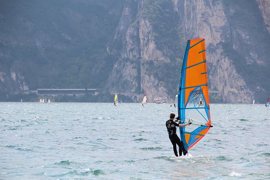 Man in Black Wetsuit Standing on Orange and Blue Sailboat during Daytime HD wallpaper