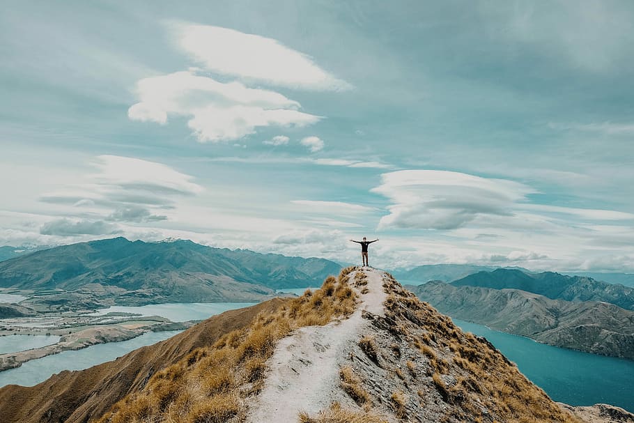 person standing on peak of the mountain near lake under white cloud blue skies, person standing near cliff HD wallpaper