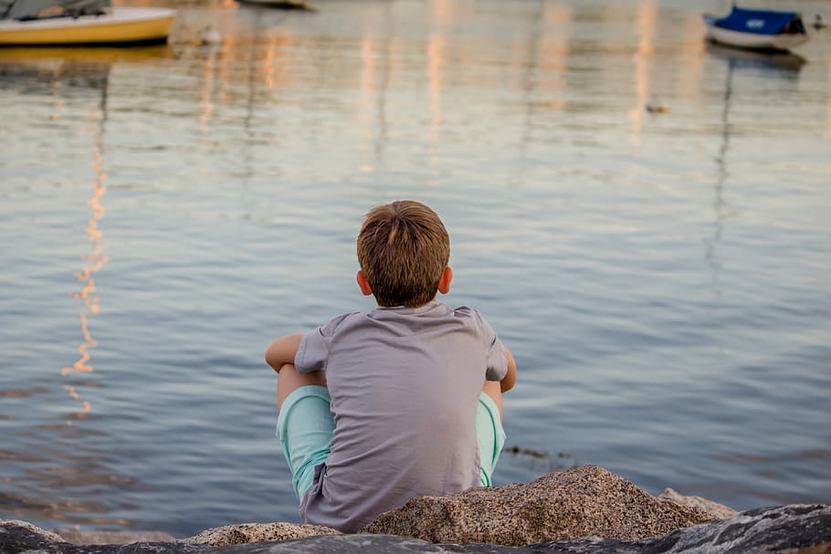 gray sitting on gray concrete pavement facing ocean water during daytime, boy sitting in front of body of water during daytime HD wallpaper