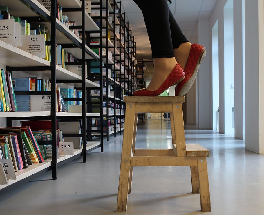 person in red shoes standing on wooden step ladder inside library HD wallpaper
