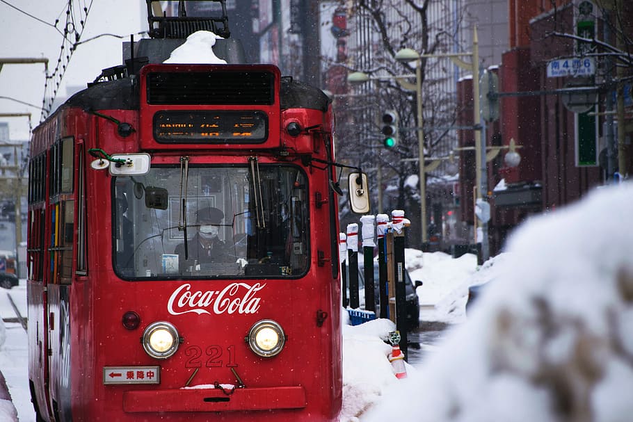 red Coca-Cola tram during snow, Coca-Cola cable train near buildings during day