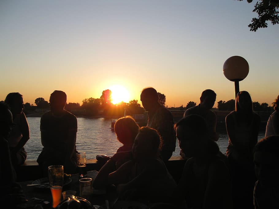 silhouette photo of people sitting beside body of water during golden hour HD wallpaper