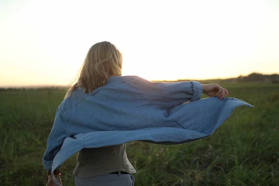 woman wearing blue denim long sleeve shirt and white pants while standing top of green grass under white sky HD wallpaper