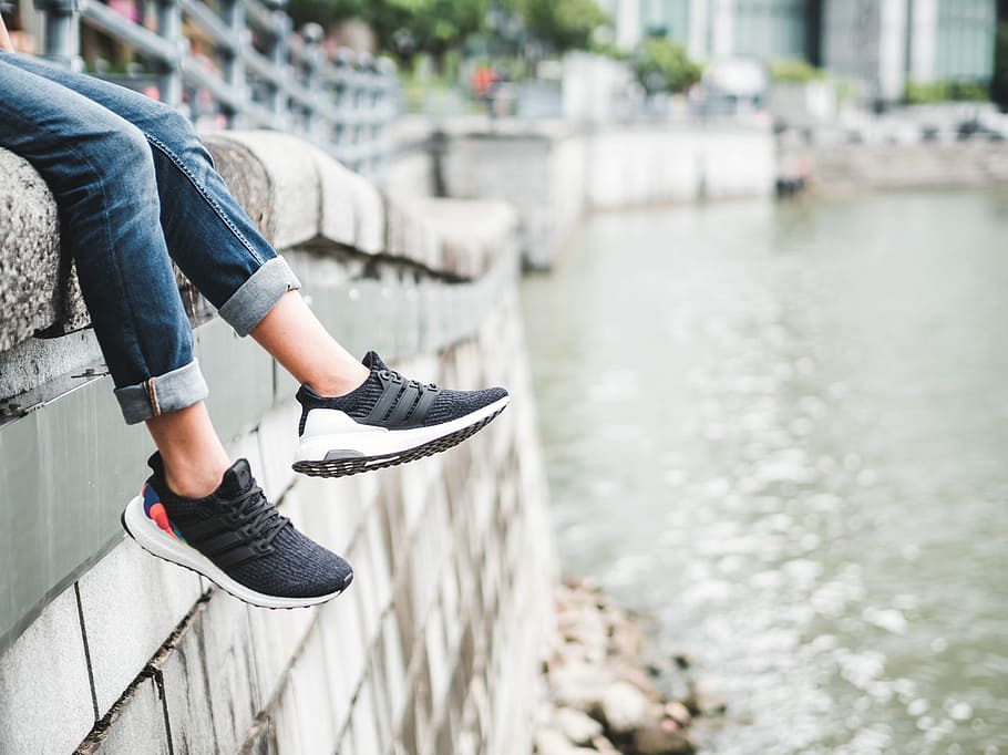 person sitting on gray ledge in front of body of water, person wearing black sneakers sits on concrete pavement, HD wallpaper