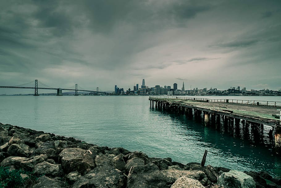gray concrete sea dock near city under white clouds during daytime, landscape photography of dock over body of water HD wallpaper