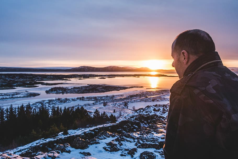 man standing on top of a mountain, man facing on trees and body of water HD wallpaper