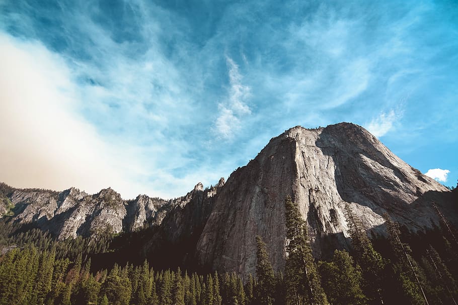 rock mountain surrounded by pine trees, brown mountain and pine trees at daytime HD wallpaper