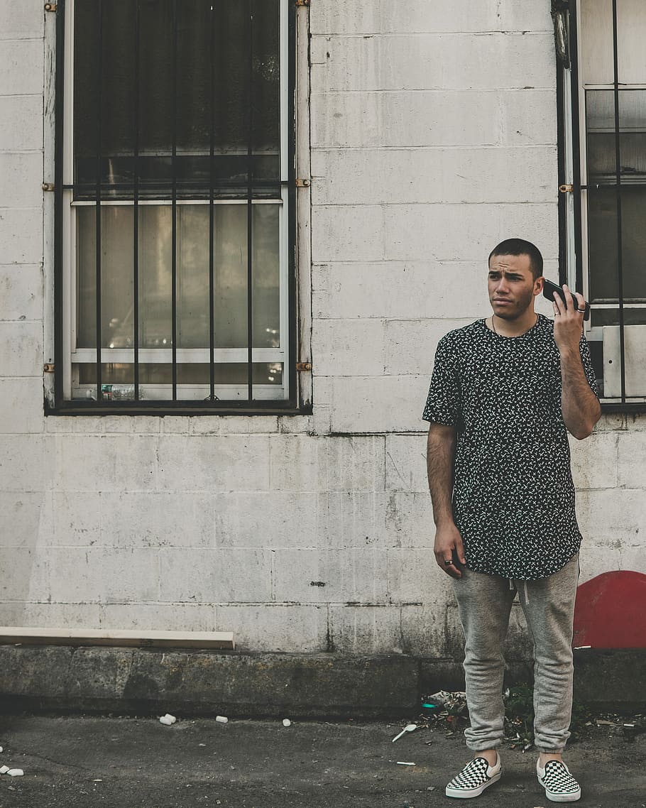 man standing in front of building while holding phone during daytime, man standing in front of wall holding smartphone near his ear HD wallpaper