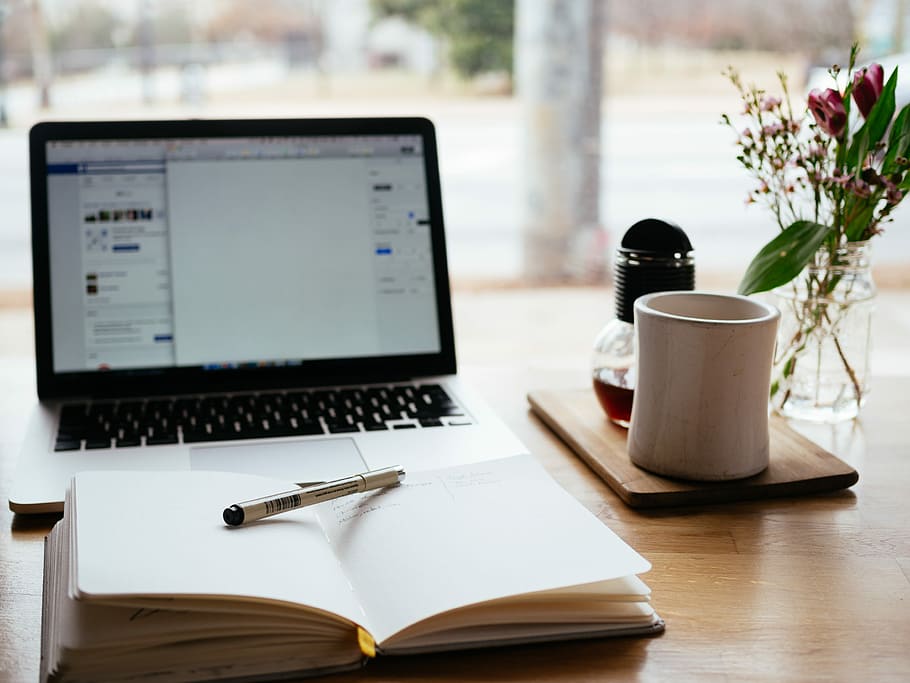 MacBook Pro near white open book, white pen on open book beside white ceramic mug HD wallpaper