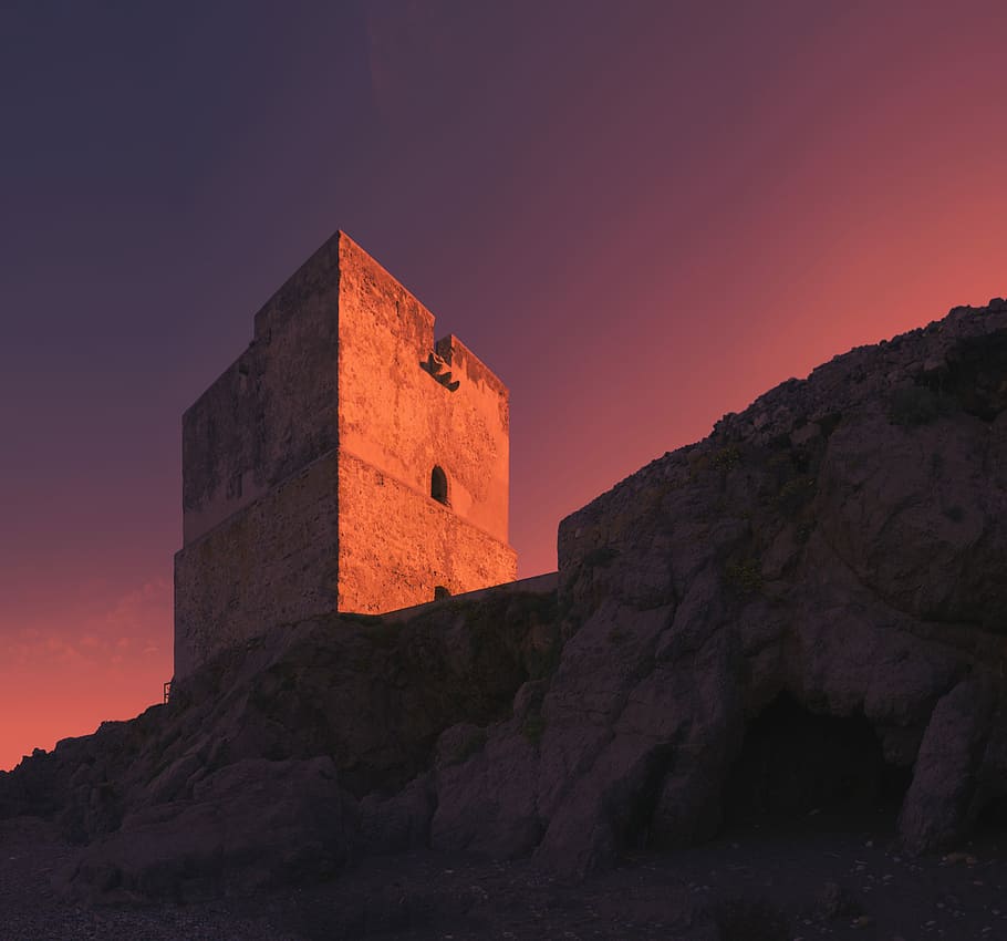 Historic coast tower beach sunset, concrete building on hilltop during sunset